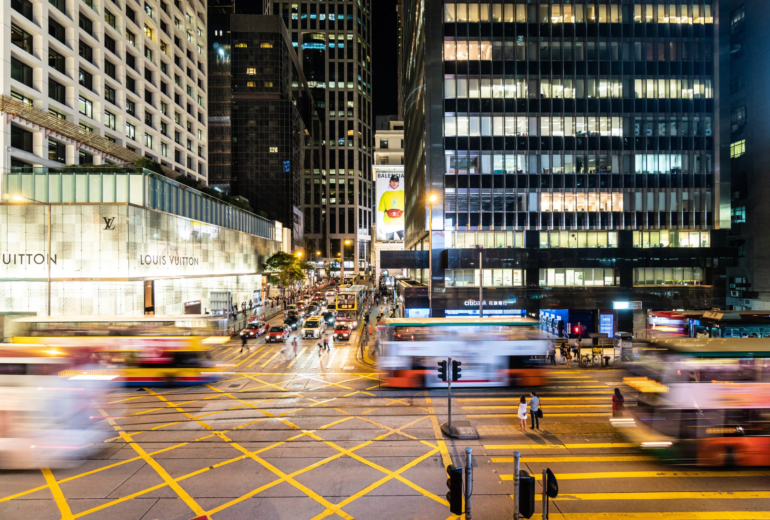 Hong Kong, China - October 8 2019: Bus and cars, captured with blurred motion, rush through a major interesection in the Central business and shopping district in Hong Kong at night